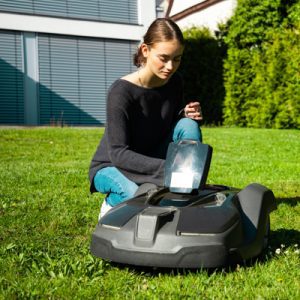 Young woman controlling robot lawn mower in summer garden